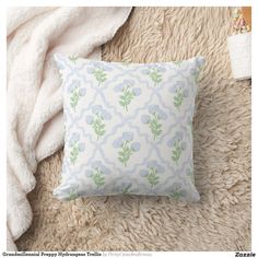 a white and blue pillow sitting on top of a fluffy rug next to a blanket