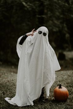 a person dressed as a ghost standing next to a pumpkin