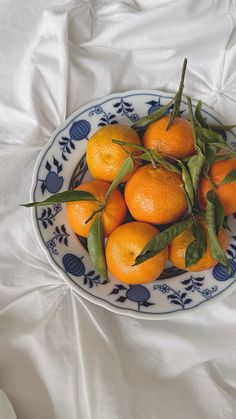 a blue and white bowl filled with oranges on top of a bed covered in sheets