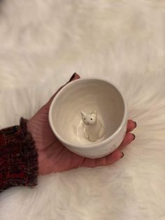 a person holding a white bowl with a small cat in the center and a tiny kitten figurine inside it