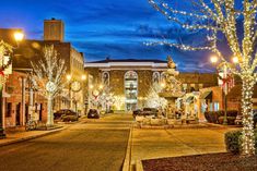 an empty street with christmas lights on the trees and cars parked in front of it