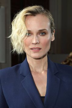 a woman with blonde hair wearing a blue suit and black shirt, looking at the camera