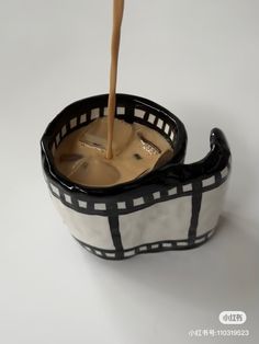 a black and white bowl filled with liquid pouring from a wooden spoon into the cup