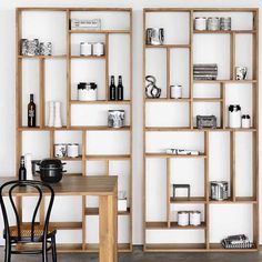 a table and chair in front of a book shelf with books on it, next to a wall mounted shelving unit