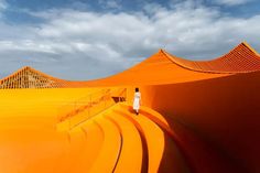 a woman standing in the middle of an orange desert with pyramids on each side