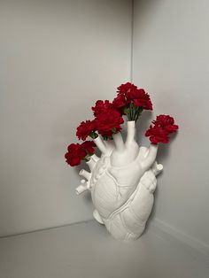 a white vase filled with red flowers sitting on top of a table next to a wall