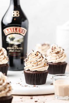 chocolate cupcakes with whipped cream frosting on a plate next to a bottle of bailey's