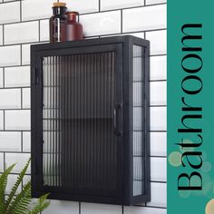 a black metal cabinet sitting on top of a white tiled wall next to a potted plant