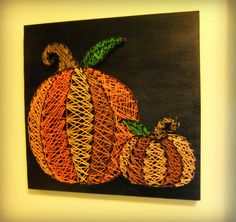 an orange and green string art pumpkin on a black background with the word fall written across it