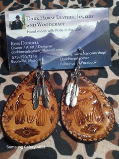 a pair of wooden earrings with metal accents on them, sitting on a camouflage background