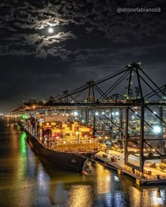 a large ship docked at night with the moon in the sky over it's horizon