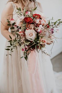 a woman in a wedding dress holding a large bouquet with red, pink and white flowers