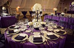 the table is set with purple linens and gold place settings, silverware, and white flowers