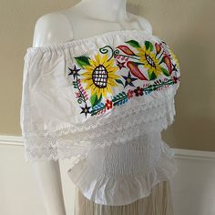 "Mexican Off shoulder elastic top with colorful sunflower embroidery. Made out of manta, 100% cotton. Color- Black/ Red and green floral embroidery. Please note: each piece is unique, the embroidery on the top and belt may be slightly different from the one pictured. Dimensions: Small Bust- 39\" Length- 20\" Medium Bust- 42\" Length- 20\" Made in Chiapas, Mexico. 🧺Care Instructions: We recommend hand washing, lay flat to dry. 📲Feel free to contact us with any questions you may have!  🛍More co Fitted Cotton Peasant Top For Beach, Festival Cotton Tops With Floral Embroidery, Multicolor Embroidered Hem Top For Vacation, Cotton Tops With Floral Embroidery For Festival, Summer Peasant Top With Multicolor Embroidery And Floral Print, Summer Festival Peasant Top With Embroidered Hem, Floral Embroidered Cotton Peasant Top For Vacation, Cotton Floral Embroidered Tops For Festivals, Fitted Cotton Peasant Top For Festivals