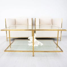 two white couches sitting next to each other on top of a glass table in front of a white wall