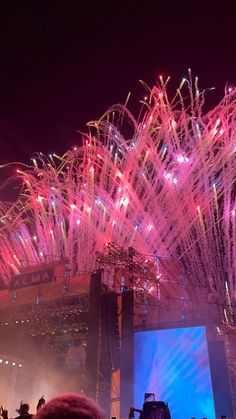 fireworks are lit up in the night sky above a stage with people standing on it