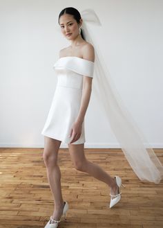 a woman in a white dress and veil walking on a hard wood floor with her legs crossed