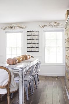 a dining room table and chairs in front of two windows with wooden planks on the wall