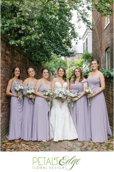 a group of women standing next to each other in front of a brick wall and trees