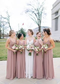 a group of women standing next to each other in front of a building holding bouquets