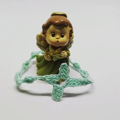 a little angel figurine sitting on top of a green crocheted chain