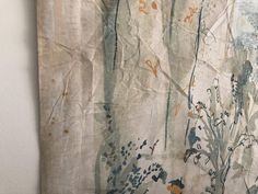 an old wall hanging on the side of a white wall with trees and flowers painted on it