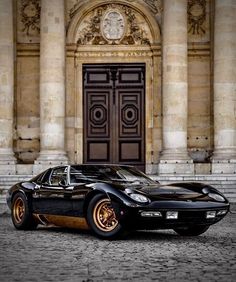 a black and gold sports car parked in front of a large building with columns on either side