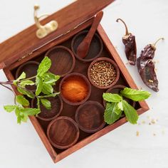 an open wooden box with spices and herbs in it on a white surface next to peppers