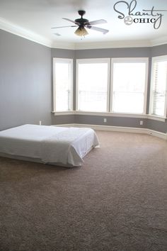 an empty bedroom with carpeted floor and ceiling fan in the corner, along with two windows