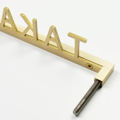 the word taka spelled in gold metal letters on a white background with a screw