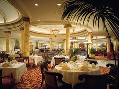 a dining room with tables and chairs covered in white tablecloths next to a palm tree