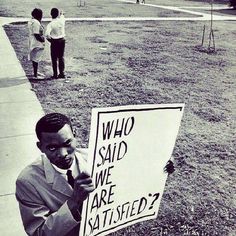 a man holding a sign that says who said we are satisfied?