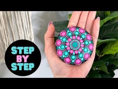 a hand holding a rock with pink and blue beads on it, in front of a plant