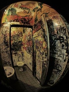 a public bathroom with graffiti all over the walls and floor, along with urinals