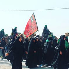 a group of people dressed in black walking down the street with one holding a flag