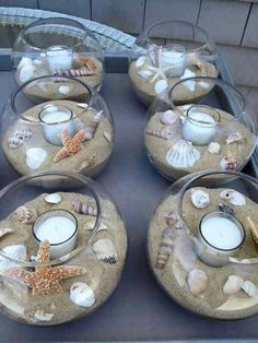 there are many candles and seashells in glass bowls on the table with sand