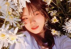 a woman with long black hair standing in front of white daisies and looking at the camera