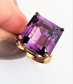 "This is one of those Statement rings with a capital \"S.\" Bold and beautiful, any purple lover or February birthday girl will be lucky to grab this one! This is a 1950s amethyst ring with an interesting arc style setting in 14K yellow gold. The attention to design in this piece is just wonderful. Simple and sculptural, it has a modern yet classic feel. The stone is about 15x16mm and estimated to weigh 14.31 carats. The amethyst is emerald cut and has a lovely translucency. Its a medium purple Timeless Formal Amethyst Ring, Formal Faceted Amethyst Ring Fine Jewelry, Luxury Faceted Amethyst Ring For Formal Events, Formal Emerald-cut Amethyst Ring, Luxury Faceted Amethyst Ring For Formal Occasions, Luxury Emerald-cut Amethyst Ring As A Gift, Luxury Classic Emerald-cut Amethyst Ring, 14k Gold Emerald-cut Amethyst Ring, 14k Yellow Gold Emerald-cut Amethyst Ring