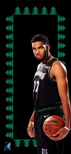 a man holding a basketball standing in front of a black and green frame with trees on it