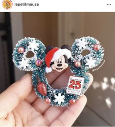 someone is holding a mickey mouse ornament with christmas decorations on it's ears