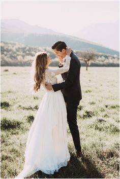 a bride and groom are standing in the grass with their arms around each other as they look at each other