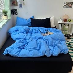 an unmade bed with blue sheets and pillows on it in a small room next to a window