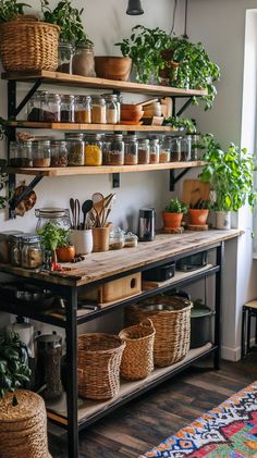 Boho kitchen with wooden shelves, black metal table, spice jars, greenery, and colorful rug on dark wood floors. Kitchen Storage No Cabinets, Unique Kitchen Shelves, Shelf With Jars, Kitchen Bakers Rack Ideas Storage, Farmers Market Kitchen Decor, Rustic Kitchen Accessories, Open Concept Kitchen Shelves, Kitchen With Plants Decor, Industrial Small Kitchen Ideas