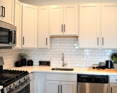 a kitchen with white cabinets, black appliances and a silver stove top oven in it