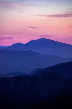 the sky is pink and purple as the sun sets in the distance over mountains with snow on them