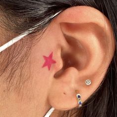 a woman's ear with a pink star tattoo on it