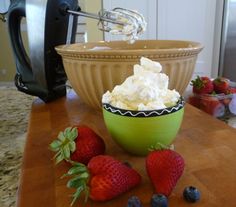 a bowl filled with whipped cream next to strawberries and blueberries on a counter