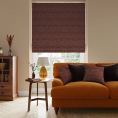 a living room with a couch, table and window covered in roman blind drapes