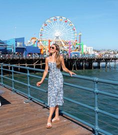 a woman standing on a pier next to the ocean with a ferris wheel in the background