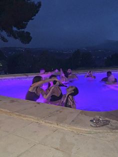 people are in the pool at night with purple lights on them and one person is taking a photo